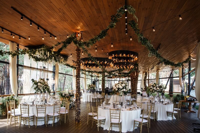 Salle de réception sous une charpente en bois, avec guirlandes lumineuses et tables rondes