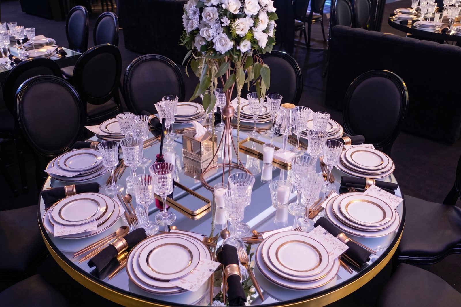 Table ronde dressée avec des verres en cristal, des assiettes et un bouquet de fleurs blanches